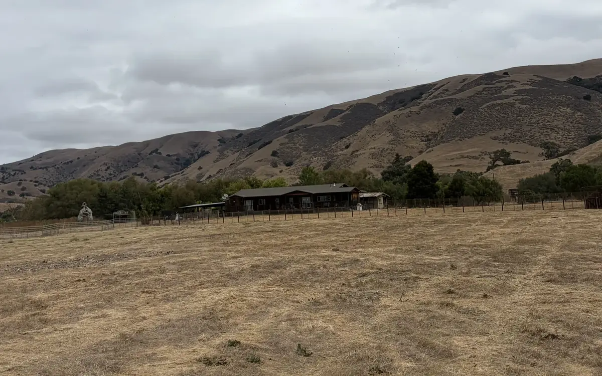 Big pasture mowed short in front of ranch buildings and dry hills, brush mowing